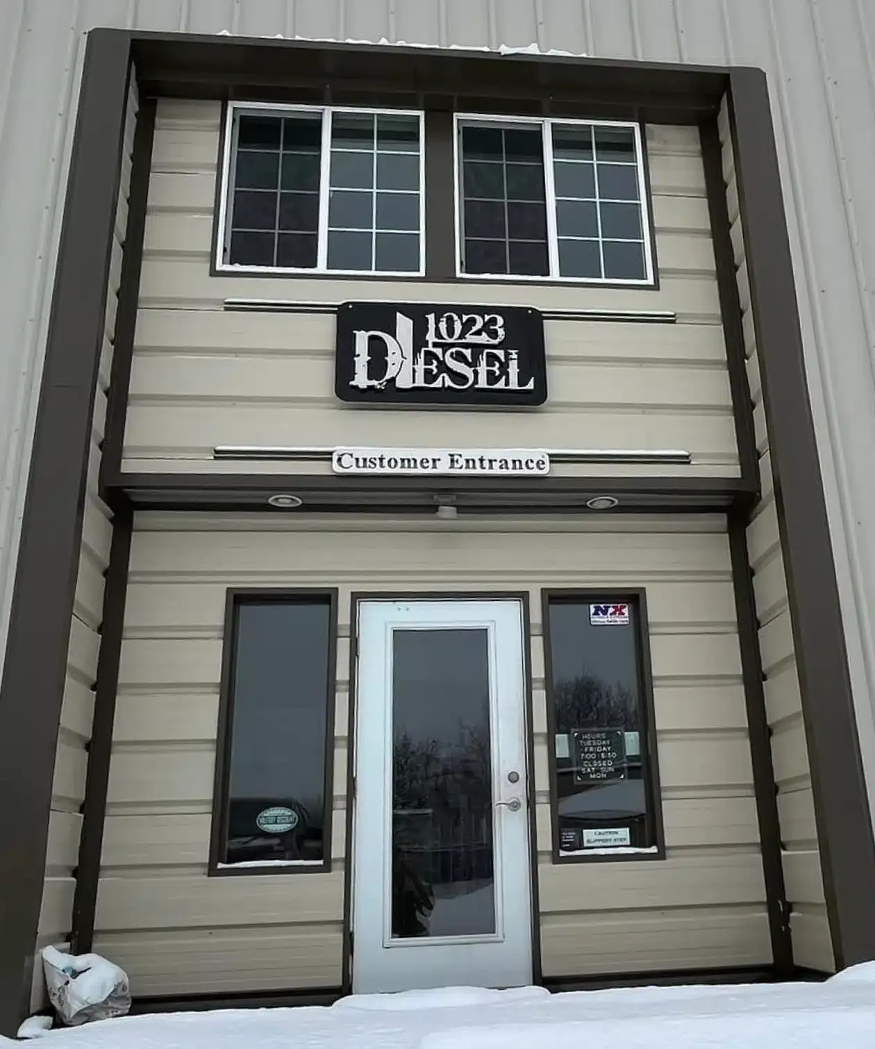 Entrance to the 1023 Diesel building with the customer entrance sign above the door and snow on the ground.