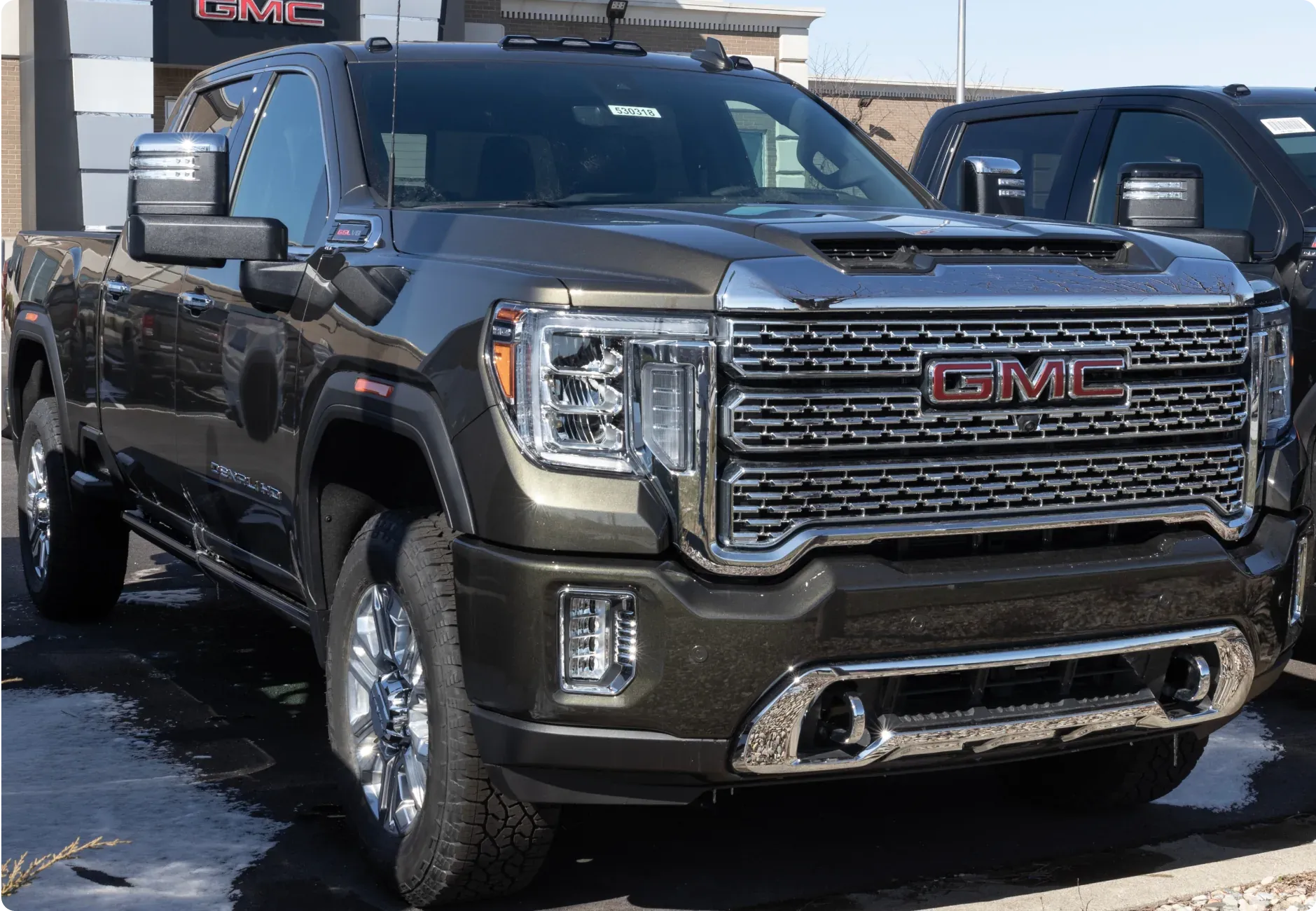 1023 Diesel & Fleet: a dark GMC Sierra 2500HD Denali pickup truck with a large chrome grille and LED headlights parked in a dealer lot.