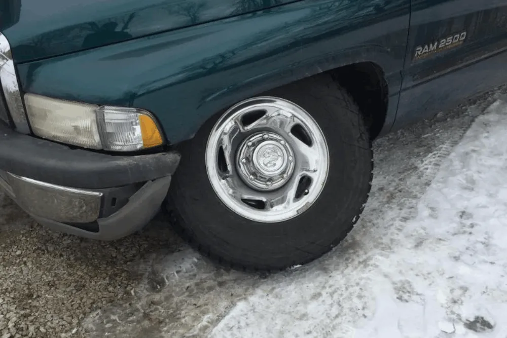 Suspension and alignment, auto repair in Palmer, AK by 1023 Diesel & Fleet. Image of a Ram 2500 front tire on icy pavement, highlighting tire wear and handling concerns that proper suspension repair and alignment help correct for safer winter driving.