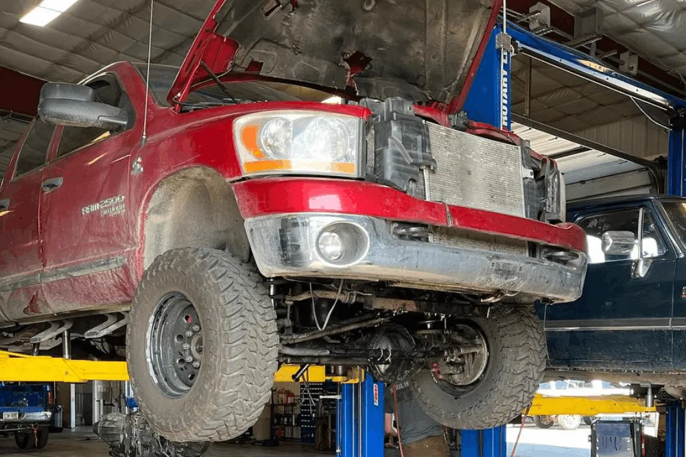 Front axle replacement and suspension repair in Palmer, AK at 1023 Diesel & Fleet. Image of a lifted Ram truck with the hood open and front suspension components exposed for service.