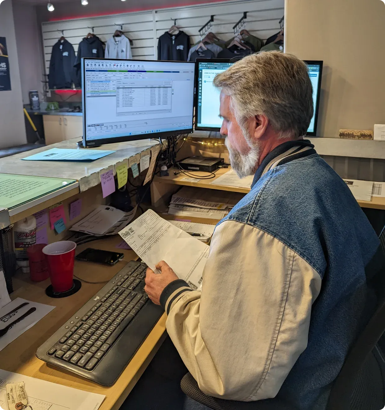 A service advisor at the 1023 Diesel & Fleet front desk with two computer monitors, holding paperwork.